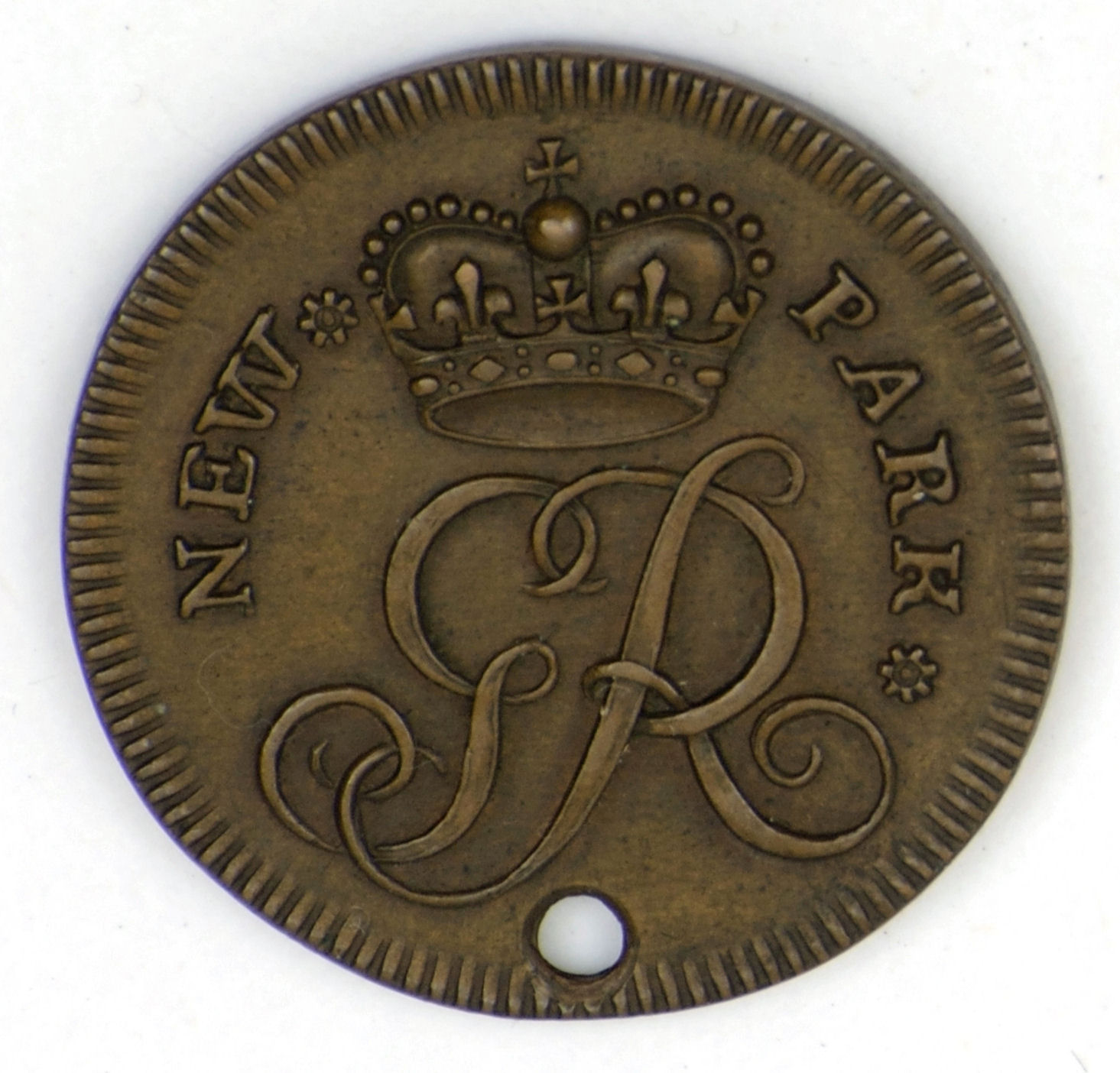 1700s bronze token carriage pass in Richmond Park, with the text "NEW PARK" and a crowned initial "GR" in ornate script. Features a decorative border and a hole near the bottom edge.