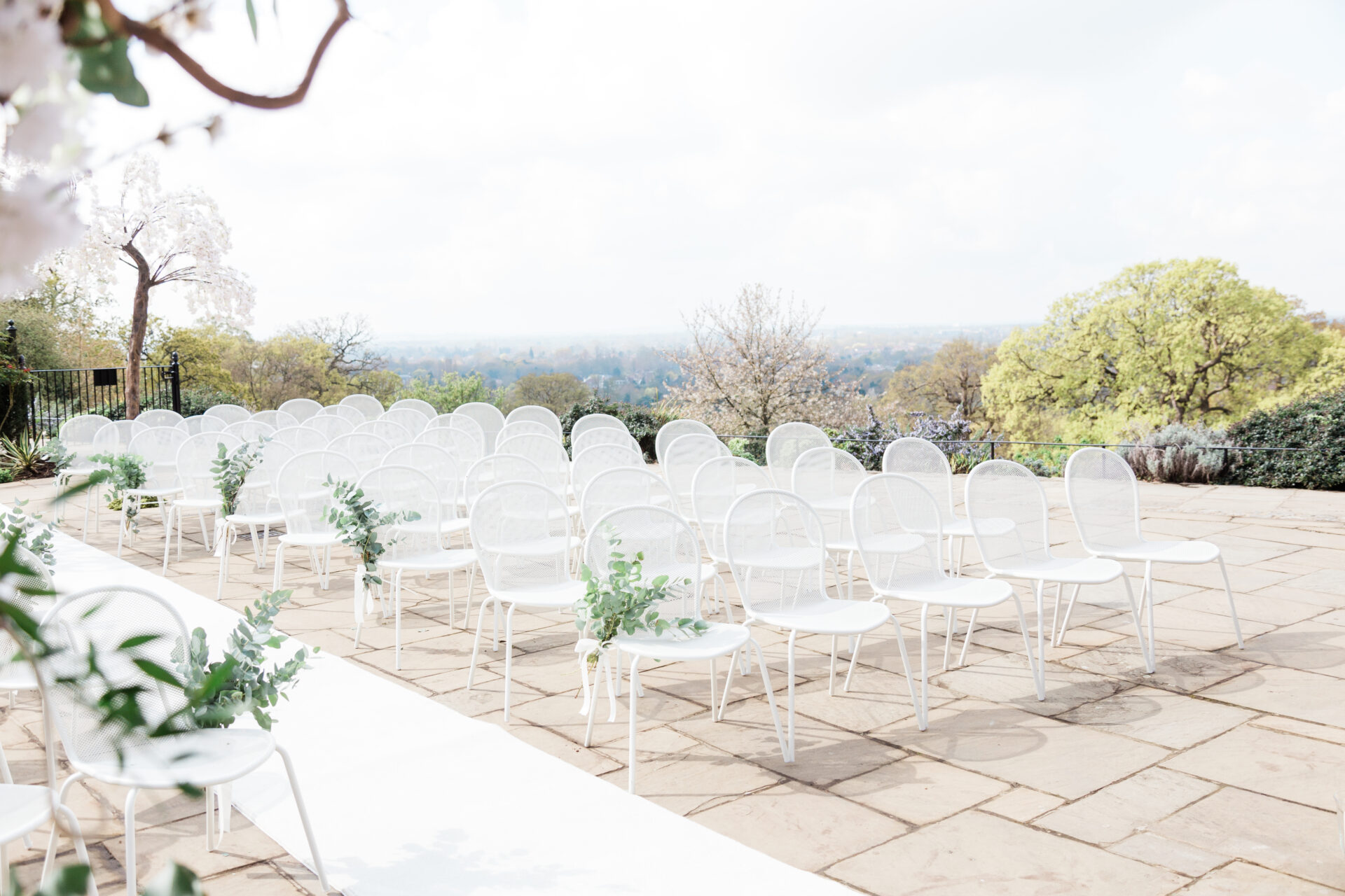 Rows of white chairs and a long white carpet on a patio.