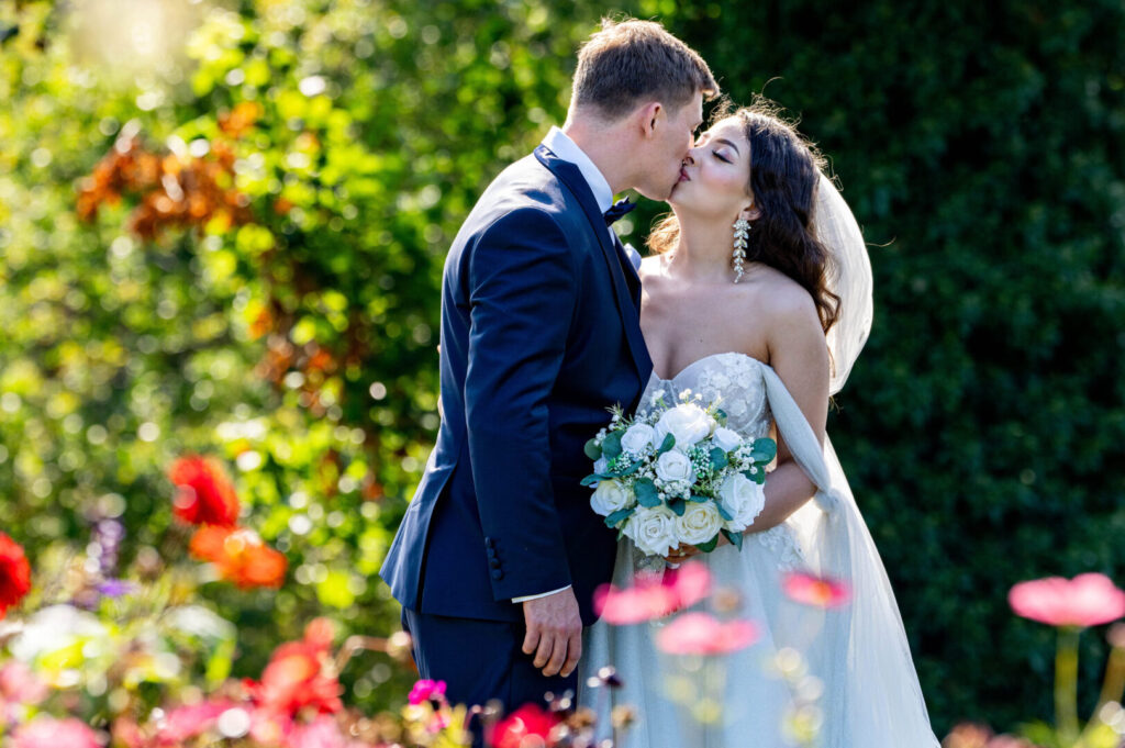 A bride and groom kissing in a garden.