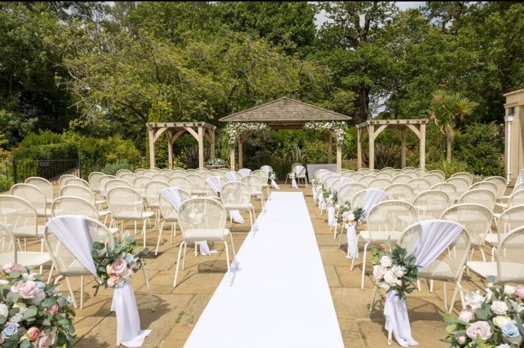 Rows of cream coloured metal chairs arranged in front of a wooden wedding arch.