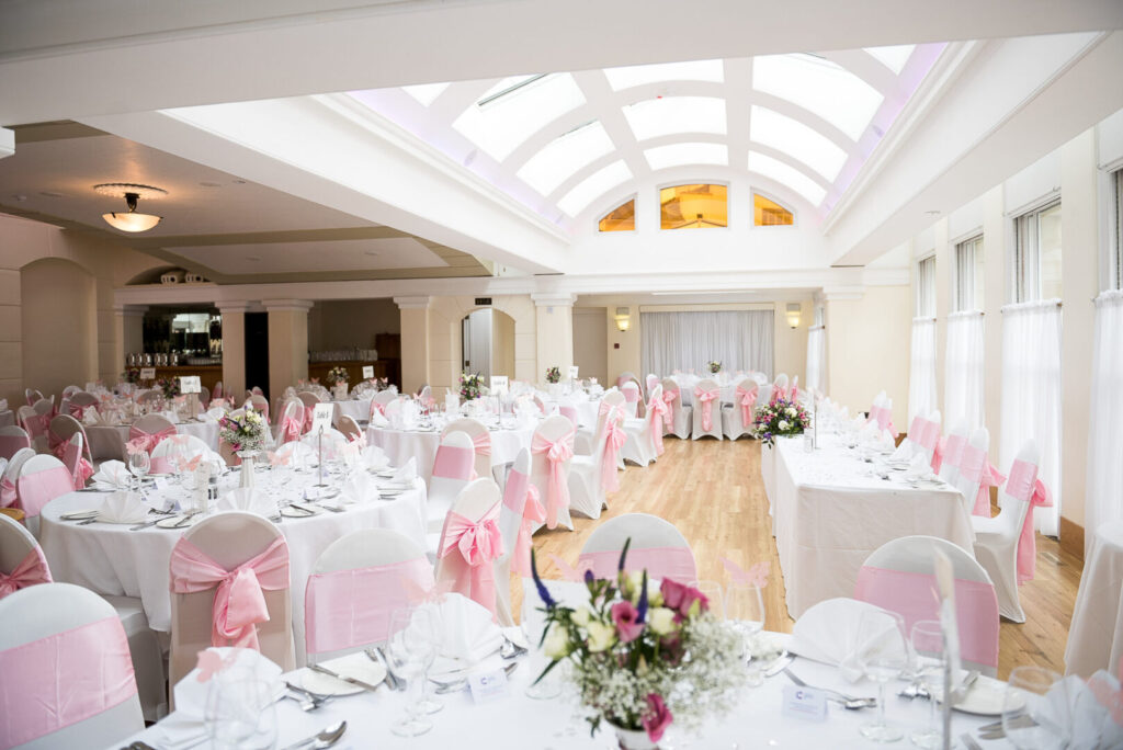 A large room with an arched roof and various shaped tables with white tablecloths.
