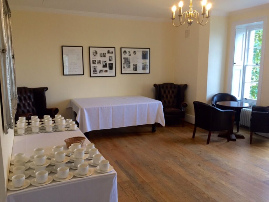 A warm room with tables dressed with white tablecloths and cups and saucers.