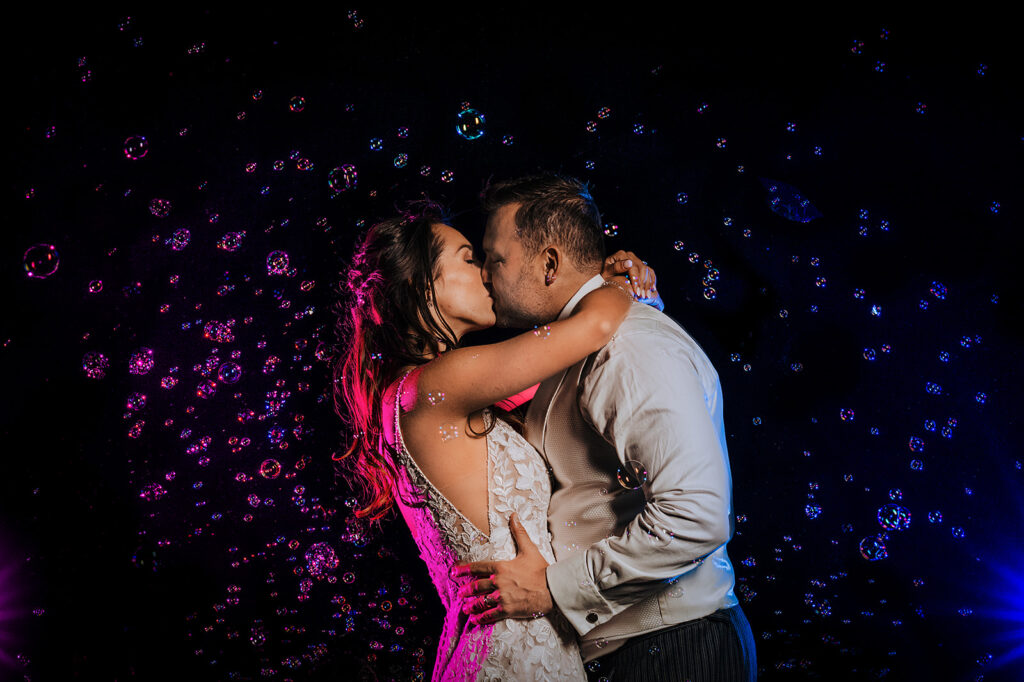 A bride and groom kiss surrounded by floating bubbles.