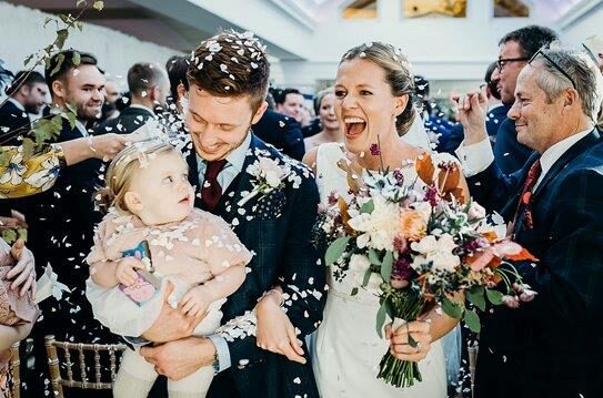 A couple and young child laughing as they're covered in confetti.