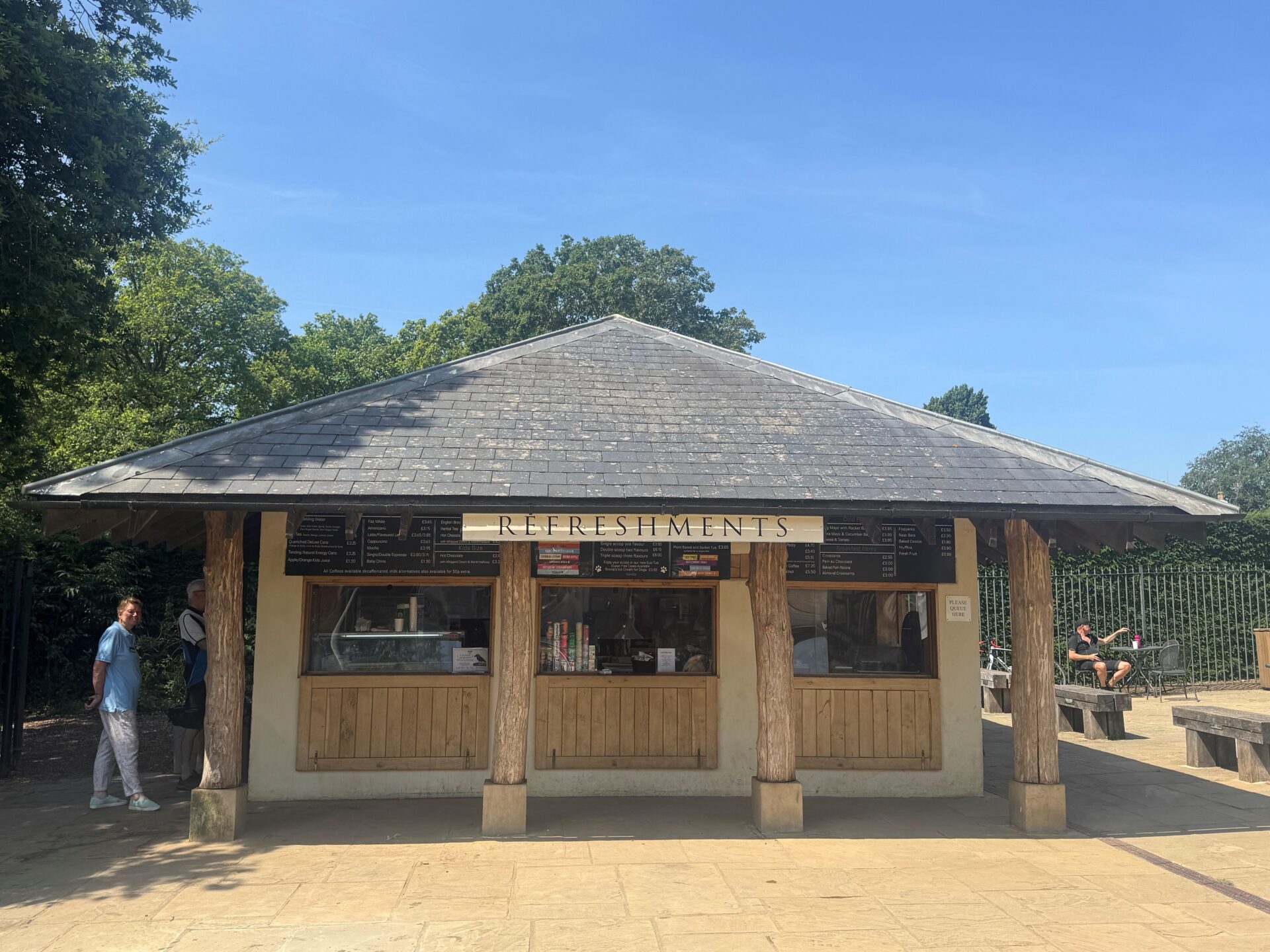 A lively refreshments kiosk in Richmond Park, where people are queuing outside for snacks and beverages on a sunny day.