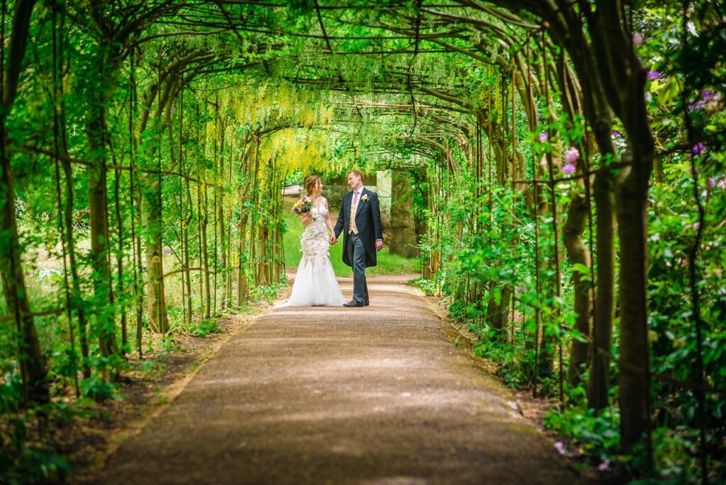 A bride and groom holding hands at the bottom of a leafy green archway.