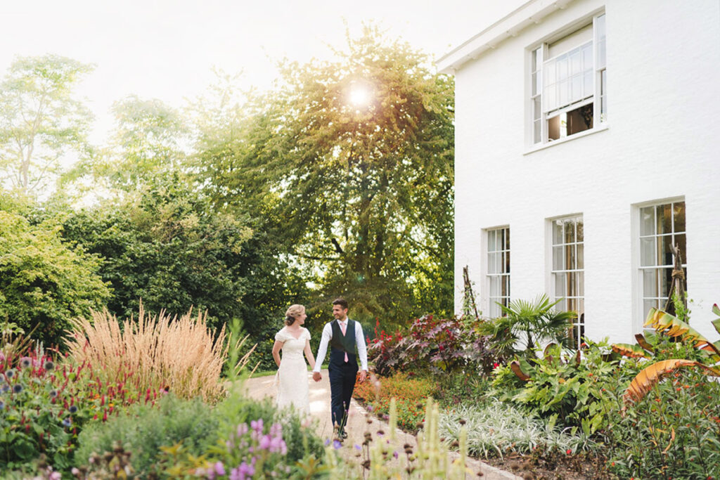 A bride and groom holding hands as they walk through a green garden.