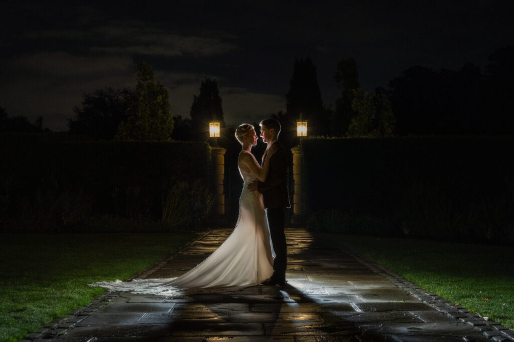 A bride and groom embracing on a stone path at night.