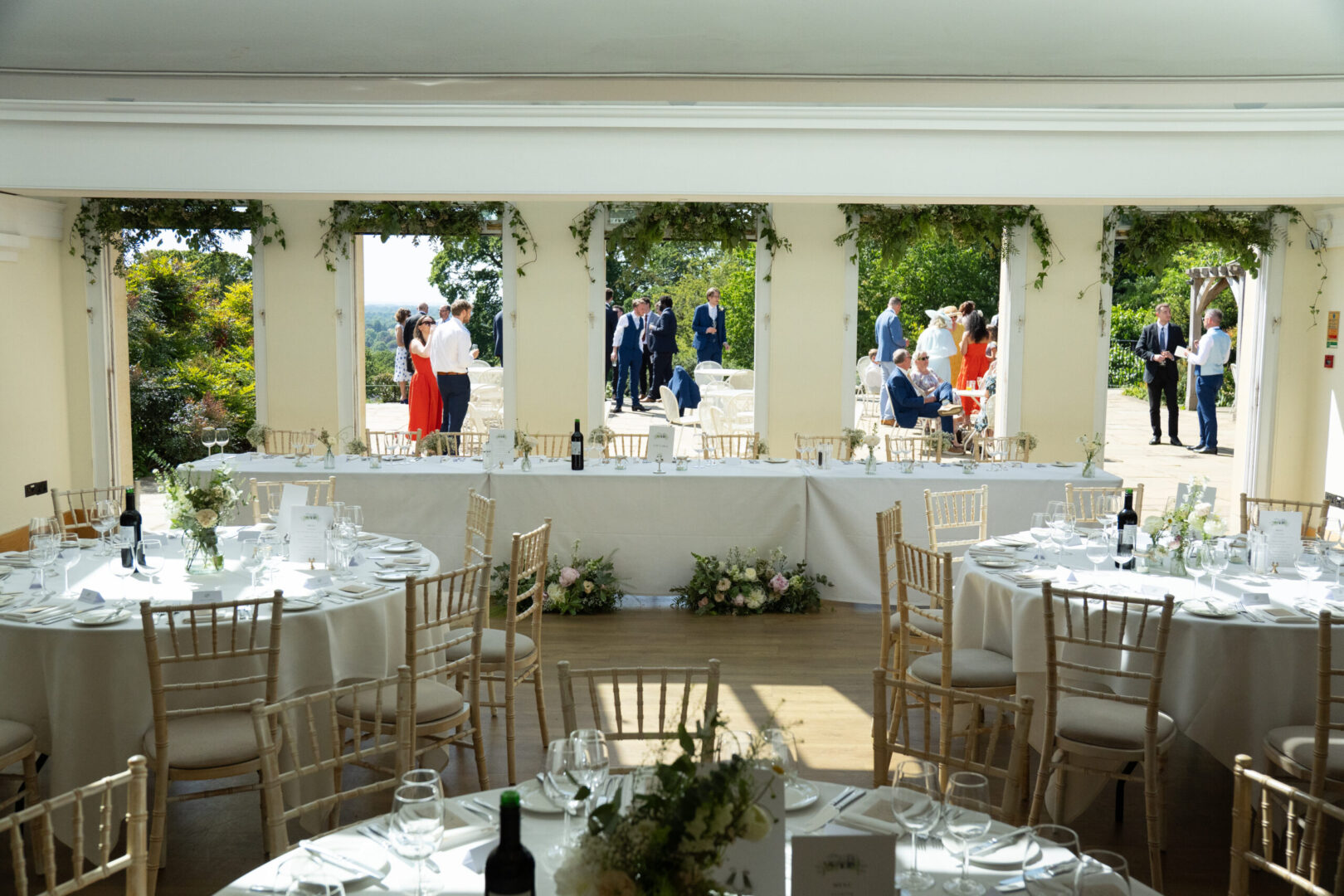A large elegant room with set tables, and doorways overlooking a busy patio.