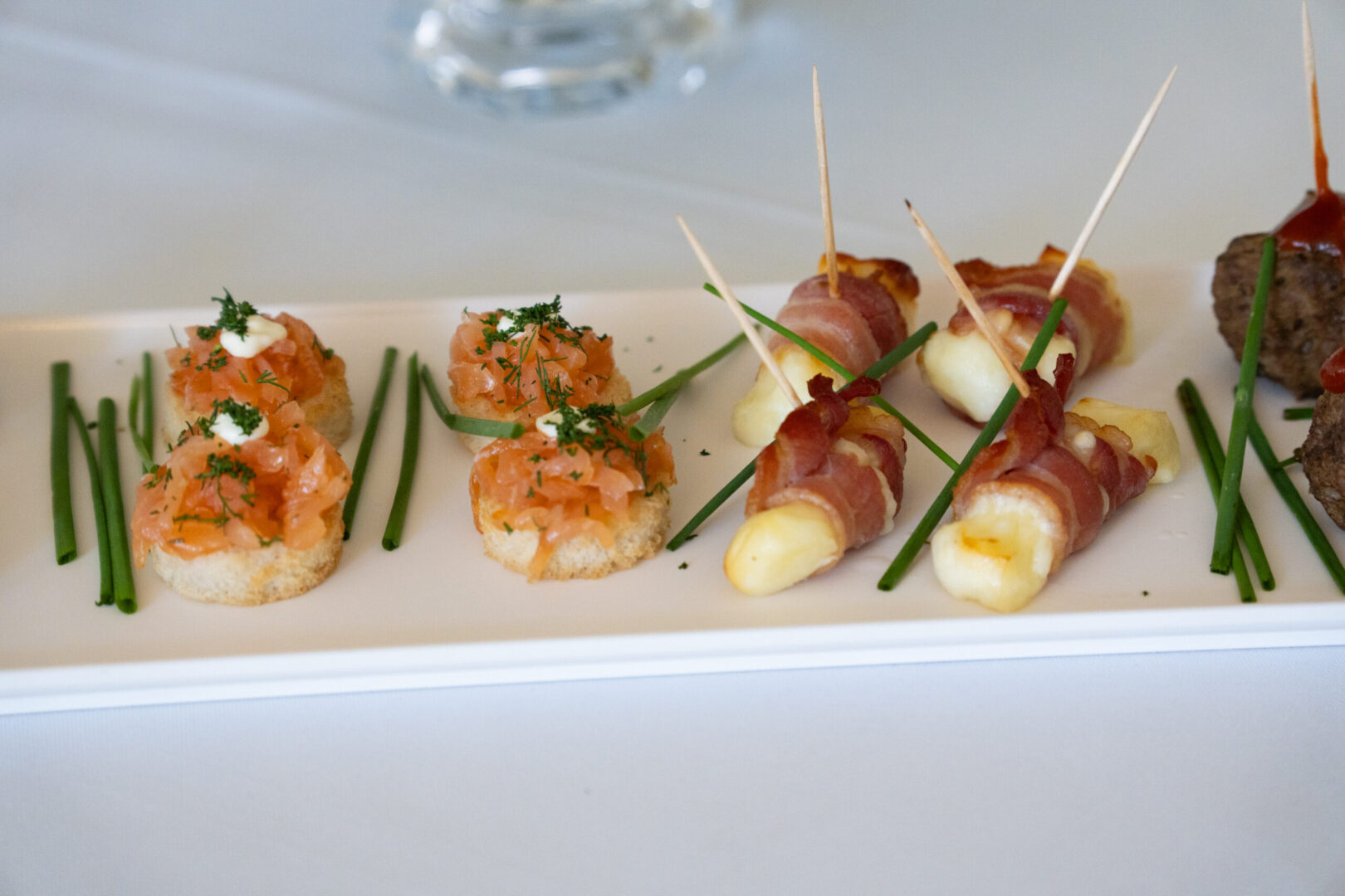 A white square plate with various hors d'oeuvres and chives.