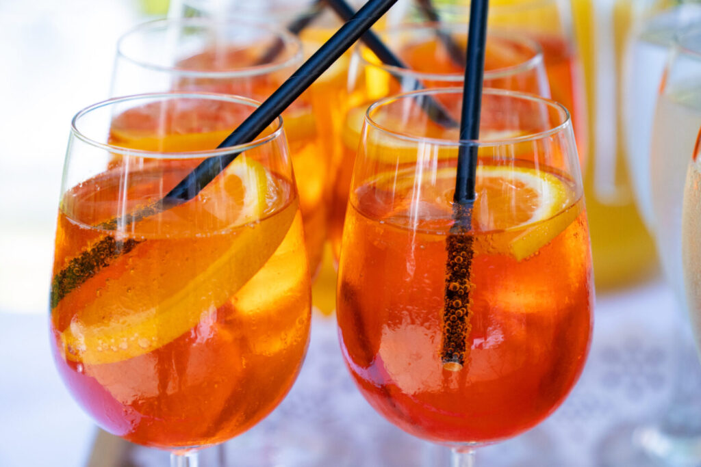 A close up of two wine glasses filled with clear orange liquid, orange slices and black straws.