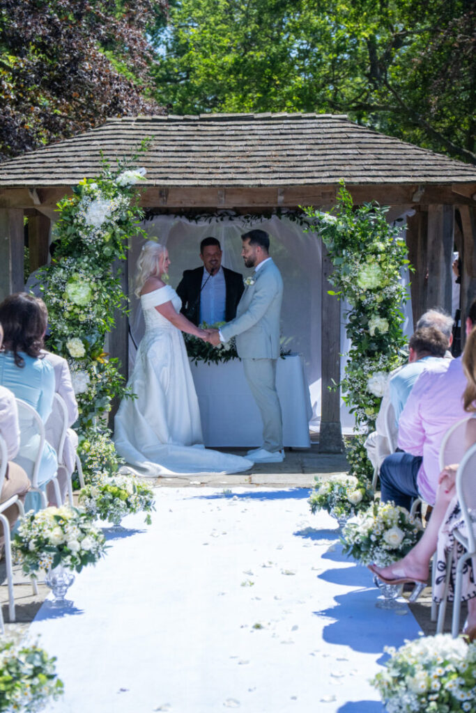 Outdoor wedding ceremony with a couple at the altar, decorated with flowers and seated guests.