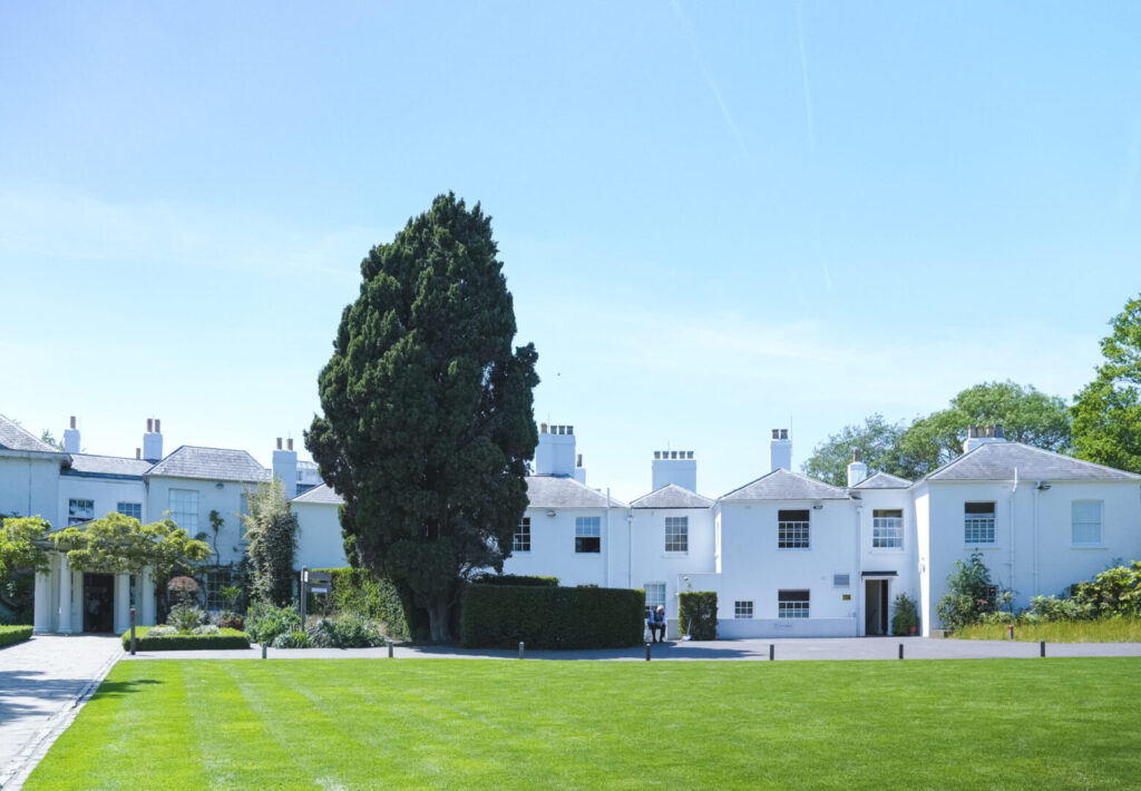 A large white Georgian house with landscaped lawns and a large tree.