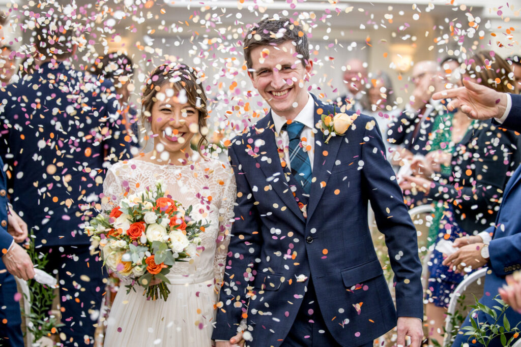 A bride and groom smiling as confetti is thrown.