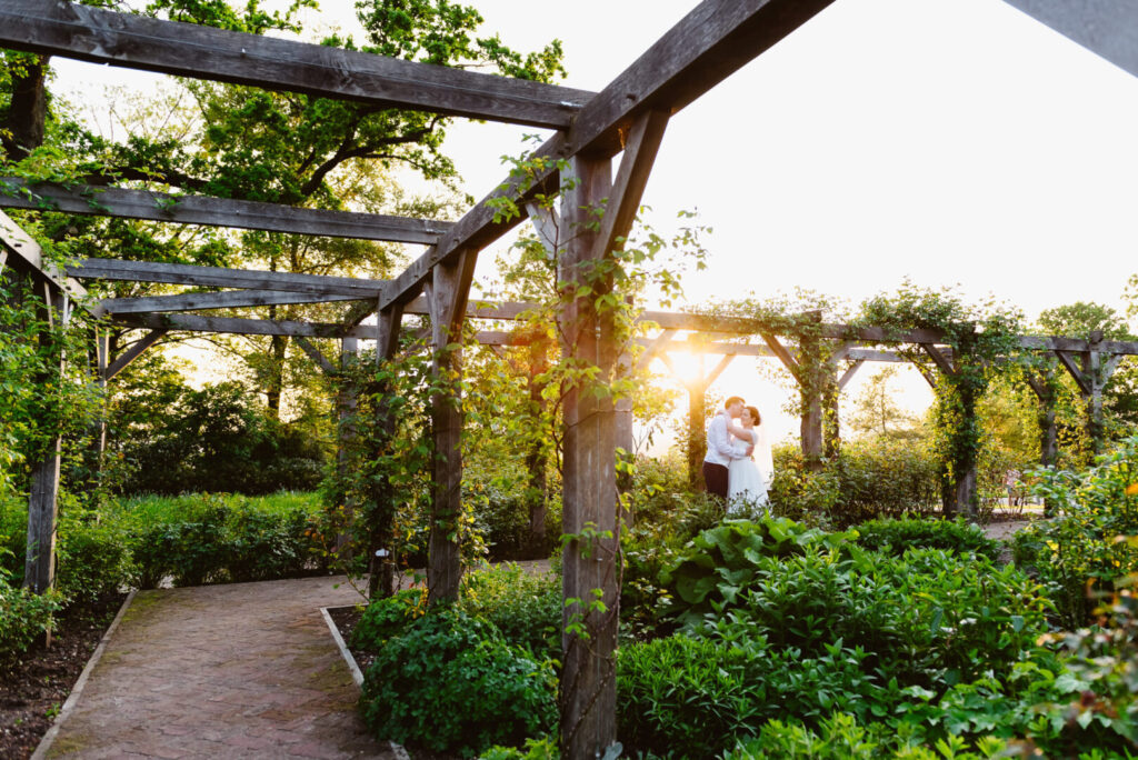 A bride and groom embracing in a vibrant garden at sunset.