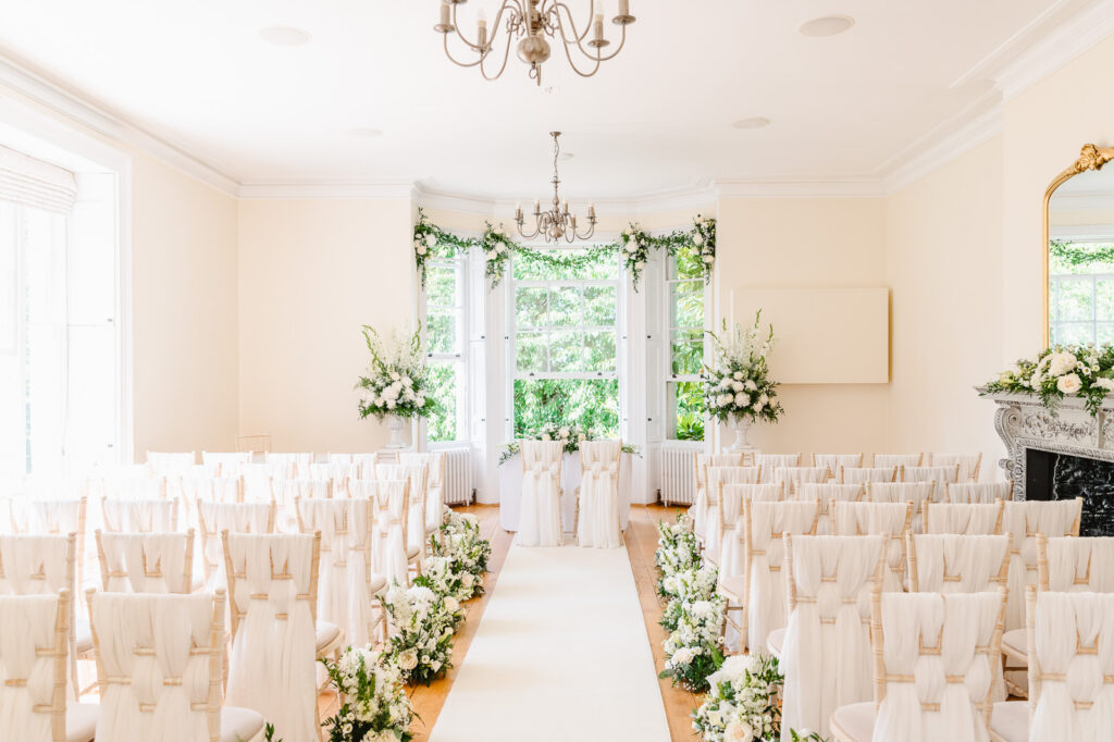 A bright room with rows of chairs with cloth and flower arrangements.