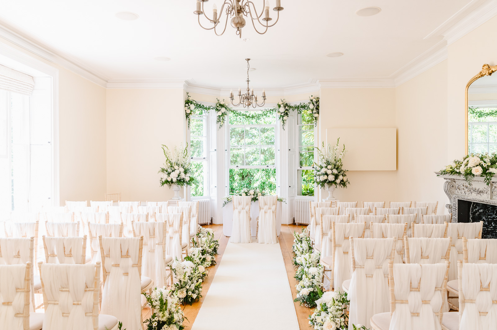 A bright room with rows of chairs with cloth and flower arrangements.