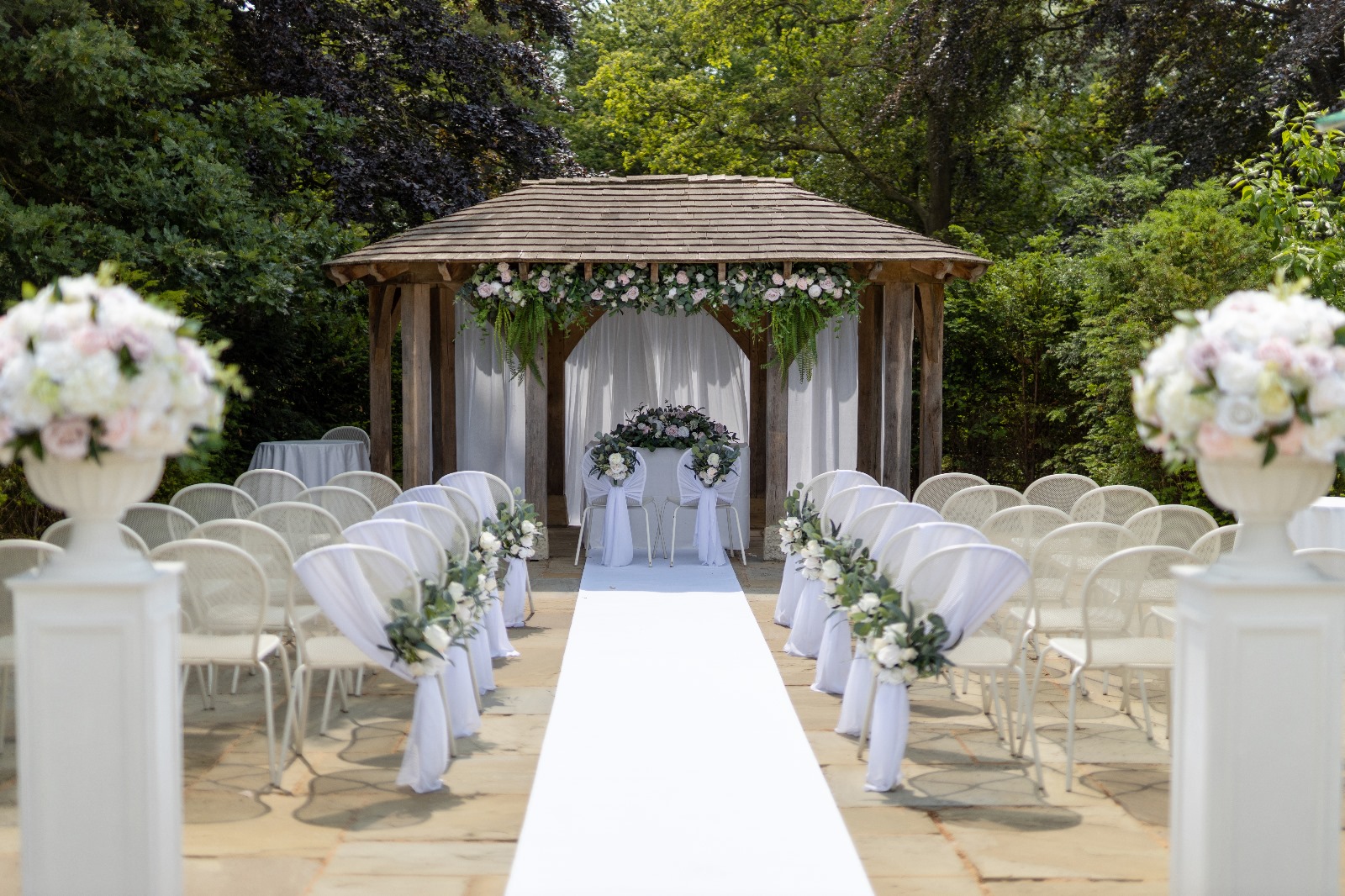 A large wooden wedding arch with rows of white chairs and a long white carpet.