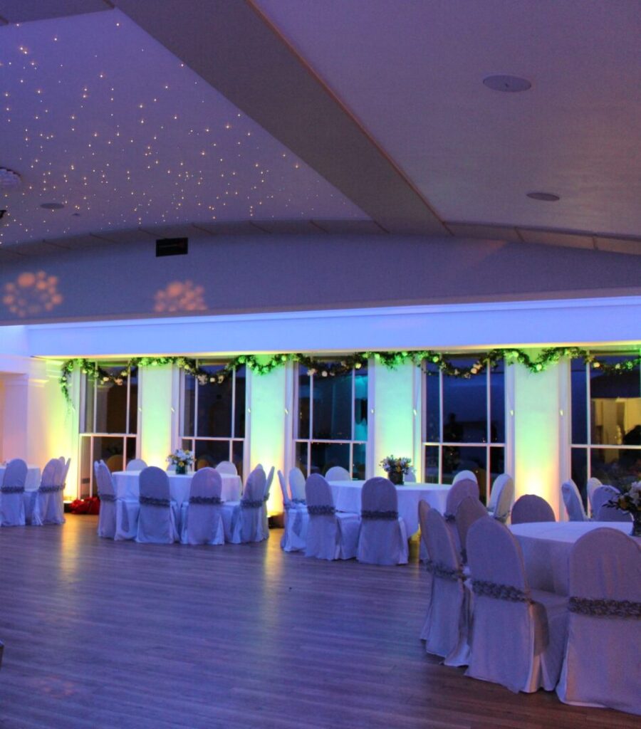 A wedding reception space at night with a large dancing space surrounded by tables and chairs.
