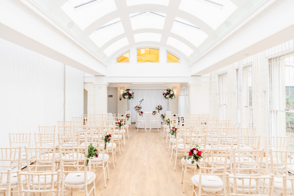 A spacious room with an arched roof and rows of wooden chairs and bright flowers.