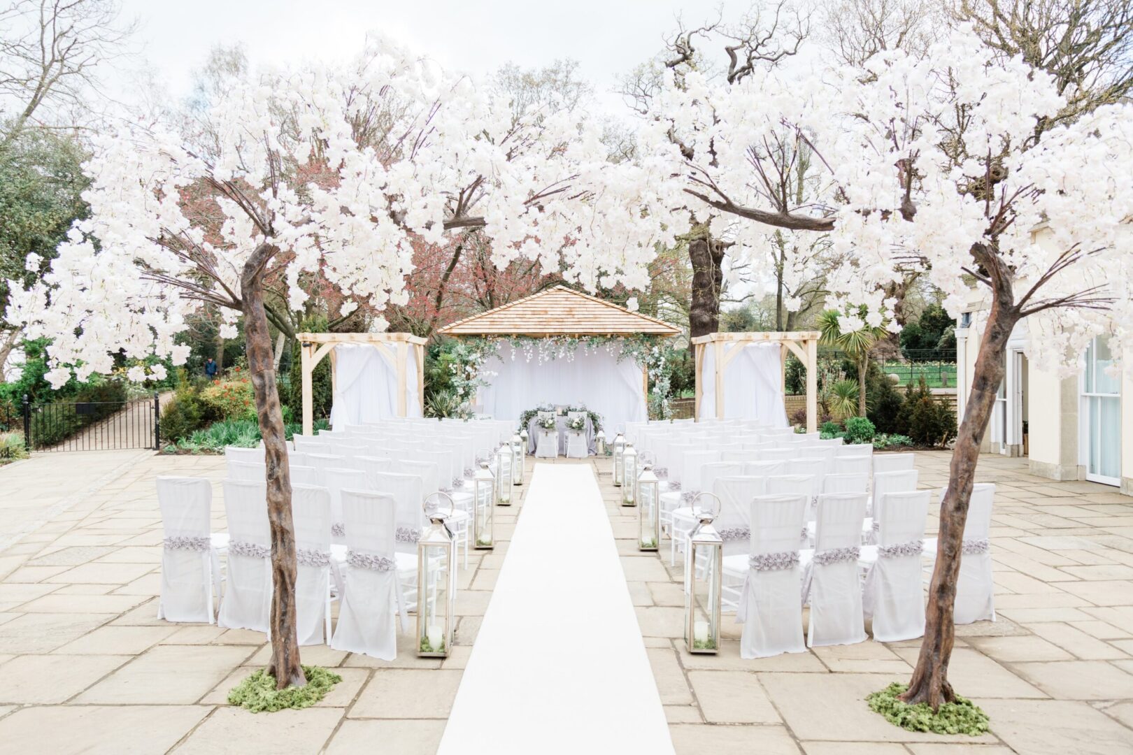 An outdoor wedding setup with white chairs and blossom trees.