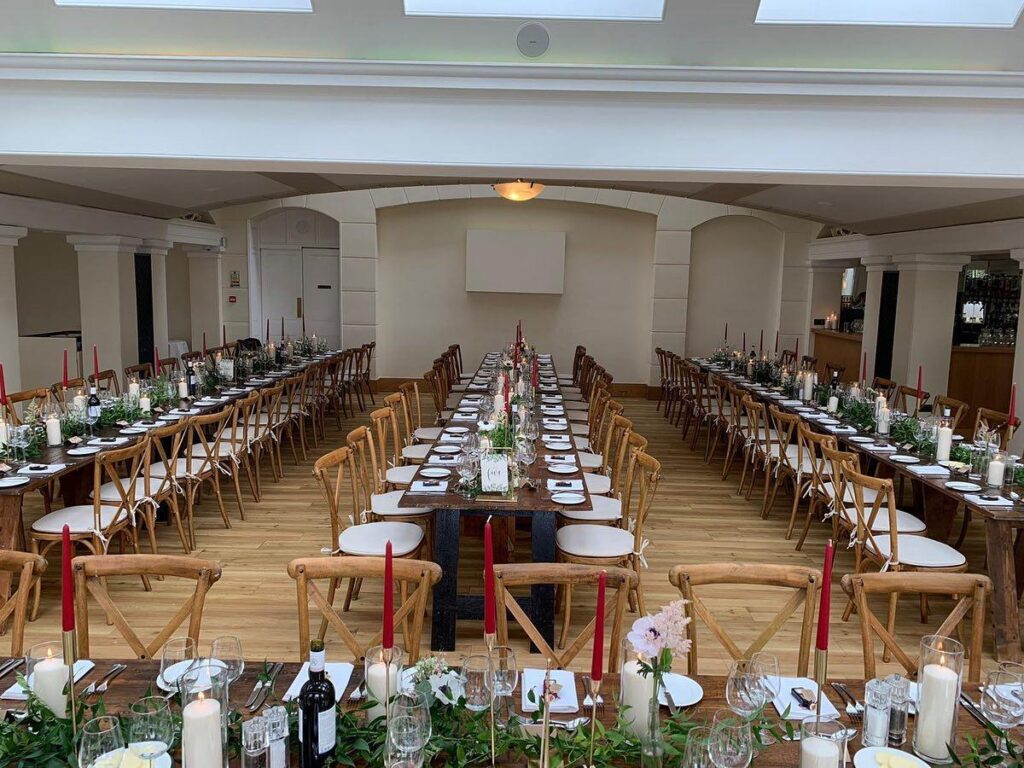 A long wedding reception table elegantly set with white linens, floral centerpieces, and place settings for guests.