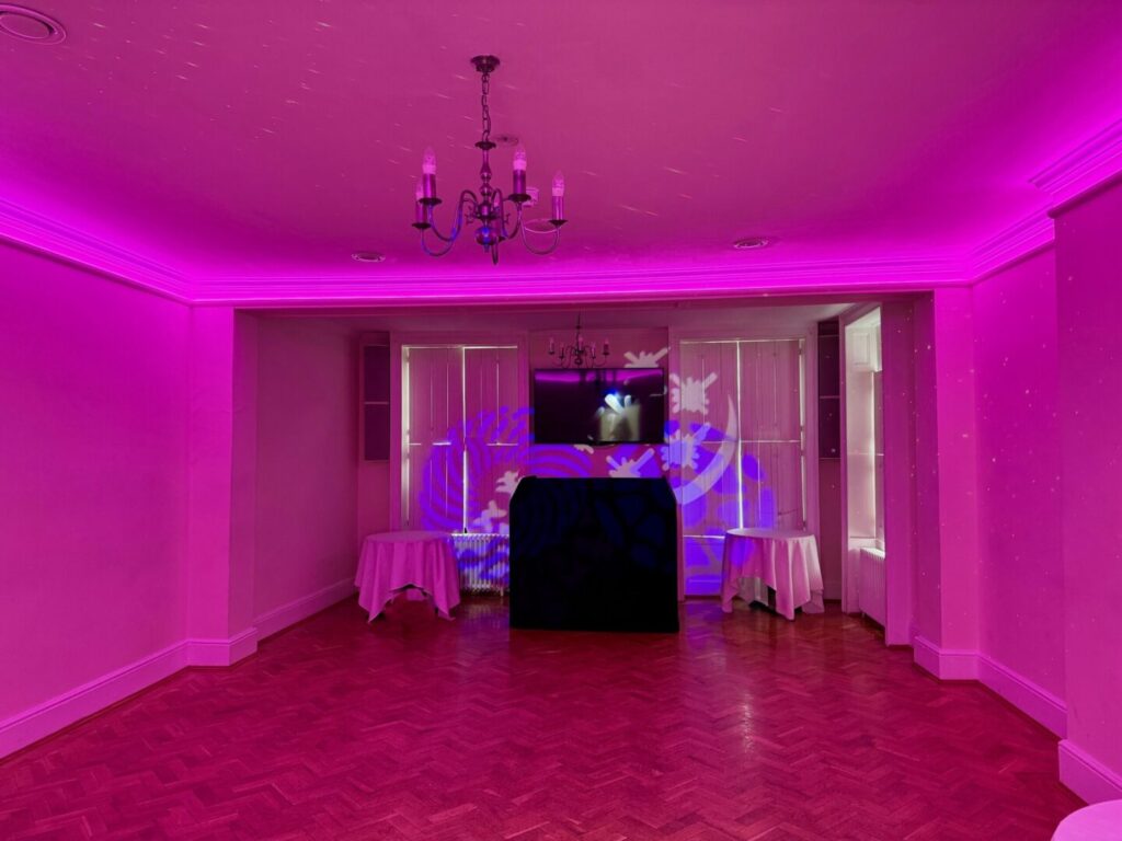 A room featuring purple lighting and an elegant chandelier hanging from the ceiling.