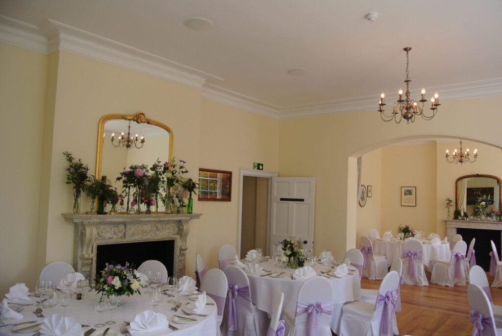 A dining room with an ornate fireplace and round tables with white tablecloths.