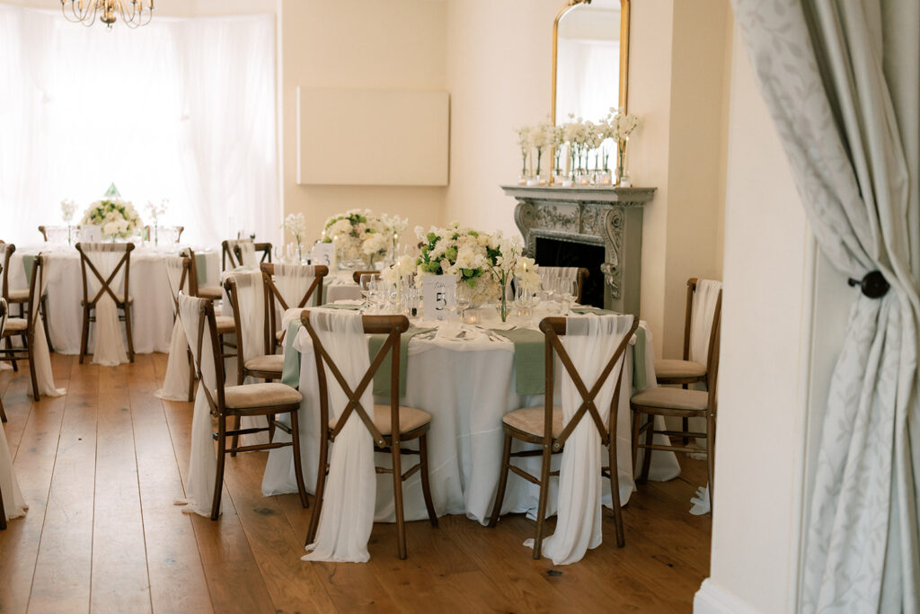 Dark wooden chairs draped with sheer white linen surrounding round tables.