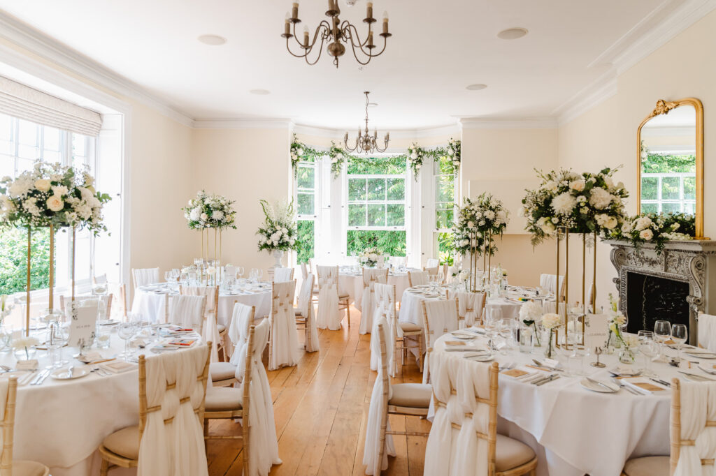 A wedding reception space with white tablecloths and vibrant floral decorations on each table.