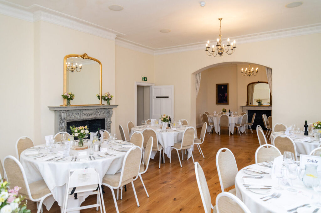A large wedding recption room with lit chandeliers and round tables.