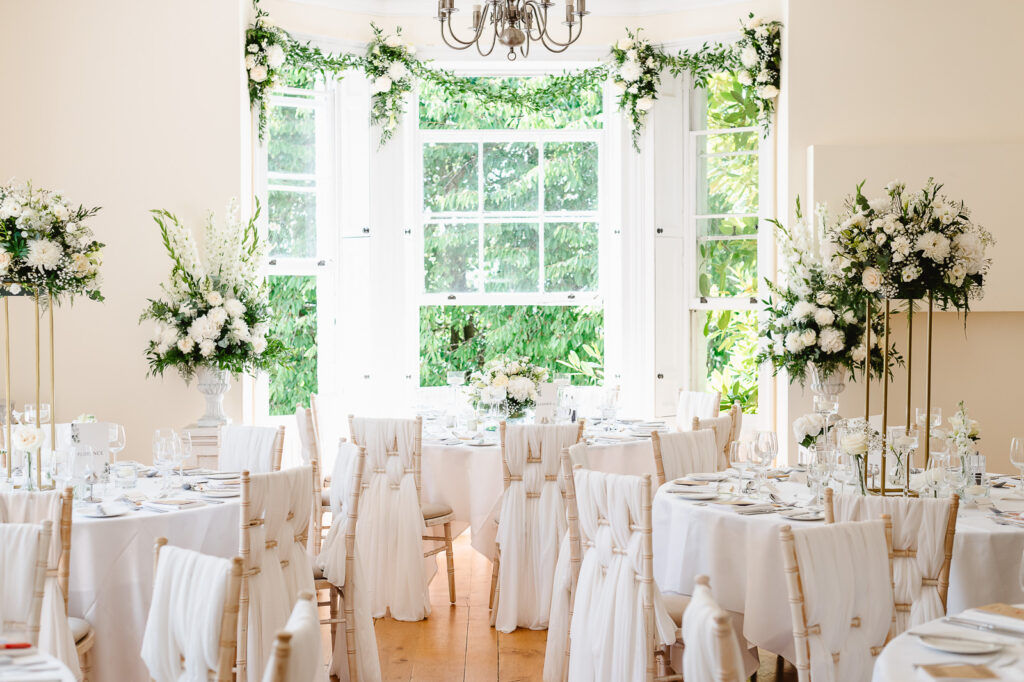 A wedding reception room featuring set tables with white tablecloths and floral centerpieces.