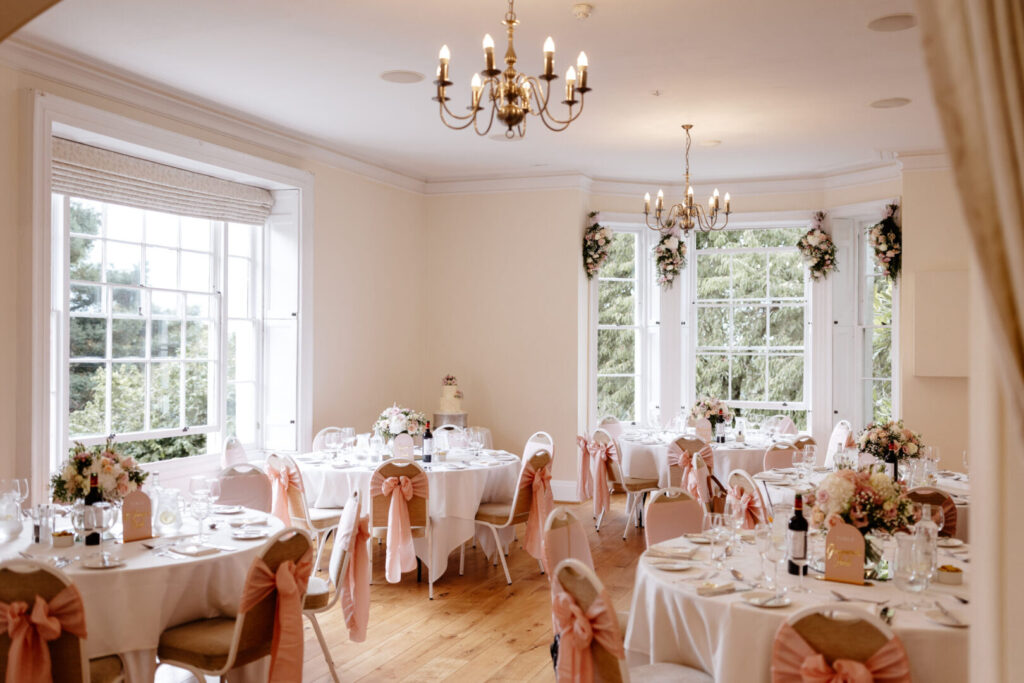 A wedding reception room featuring elegantly set tables with pink and white tablecloths.