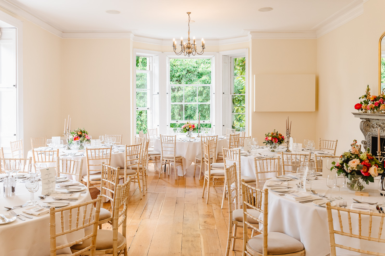 An wedding reception room showcasing white tables and chairs, set for guests with soft lighting and decor.