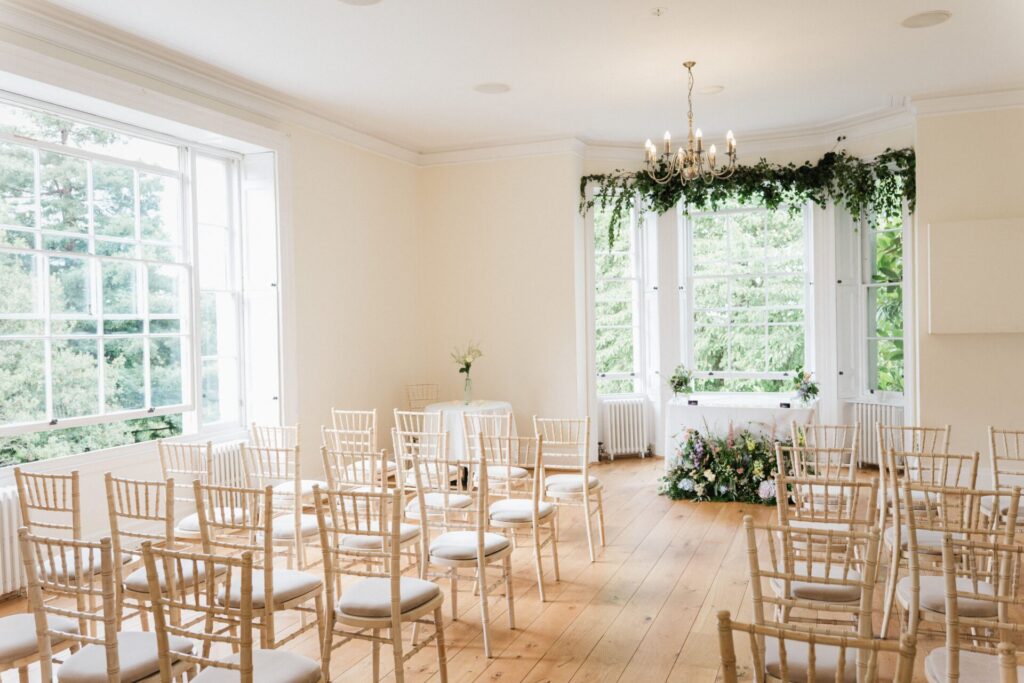 A large brightly lit room with rows of chairs and flowers over a window.