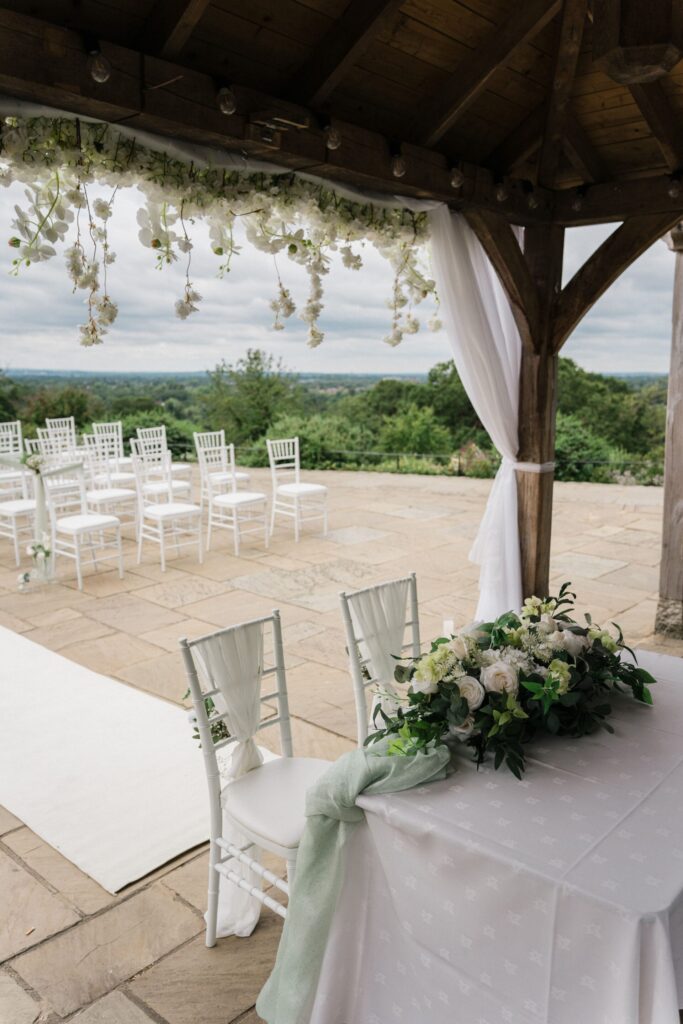 Two chairs and table under a wooden awning on a large white patio.