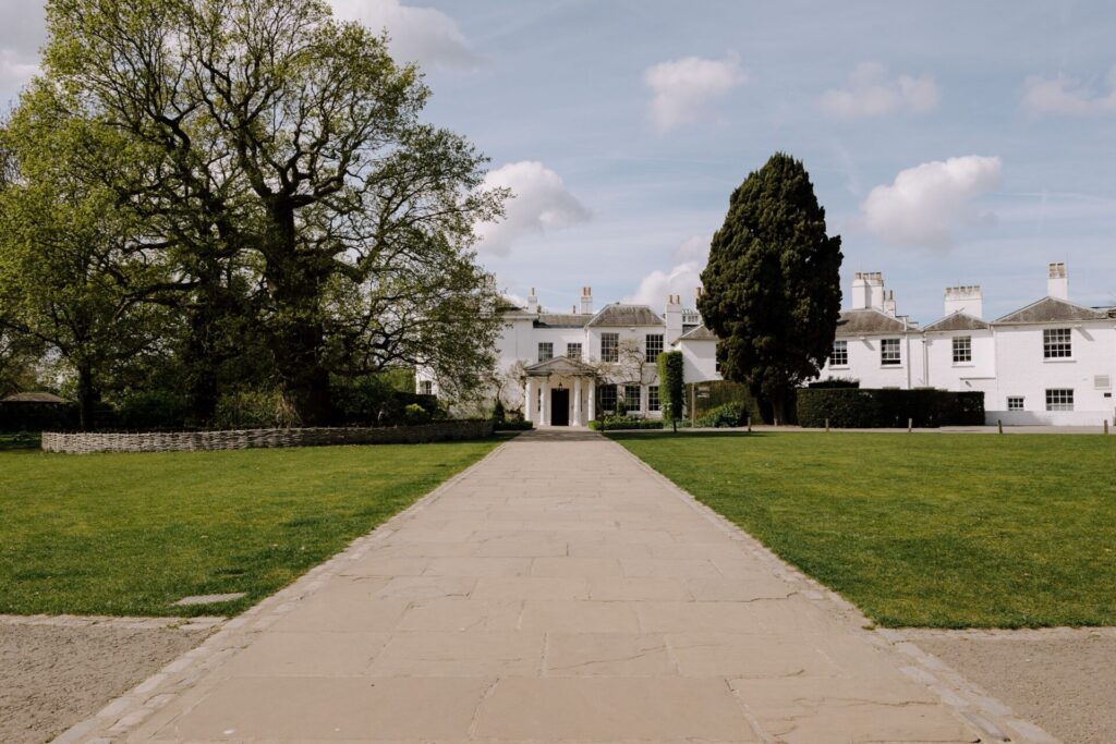 A wide angle view of a long drive leading up to a large white Georgian house.
