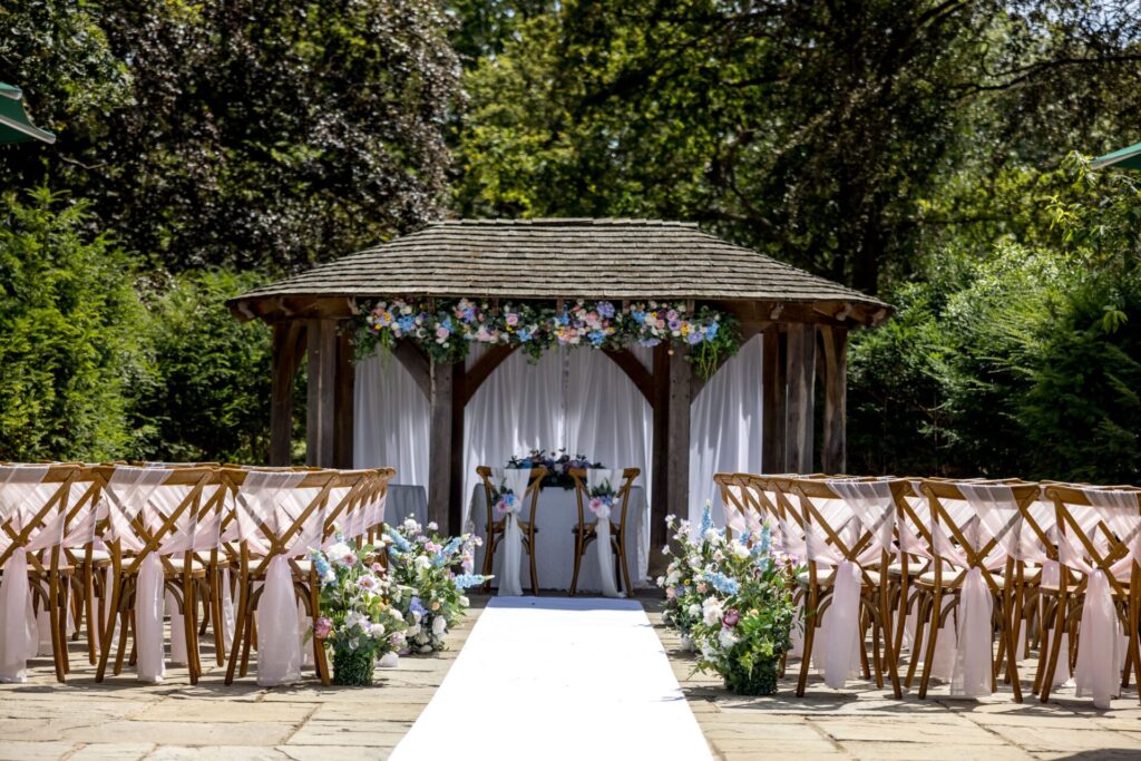 A large wooden wedding arch with rows of wooden chairs and a long white carpet.