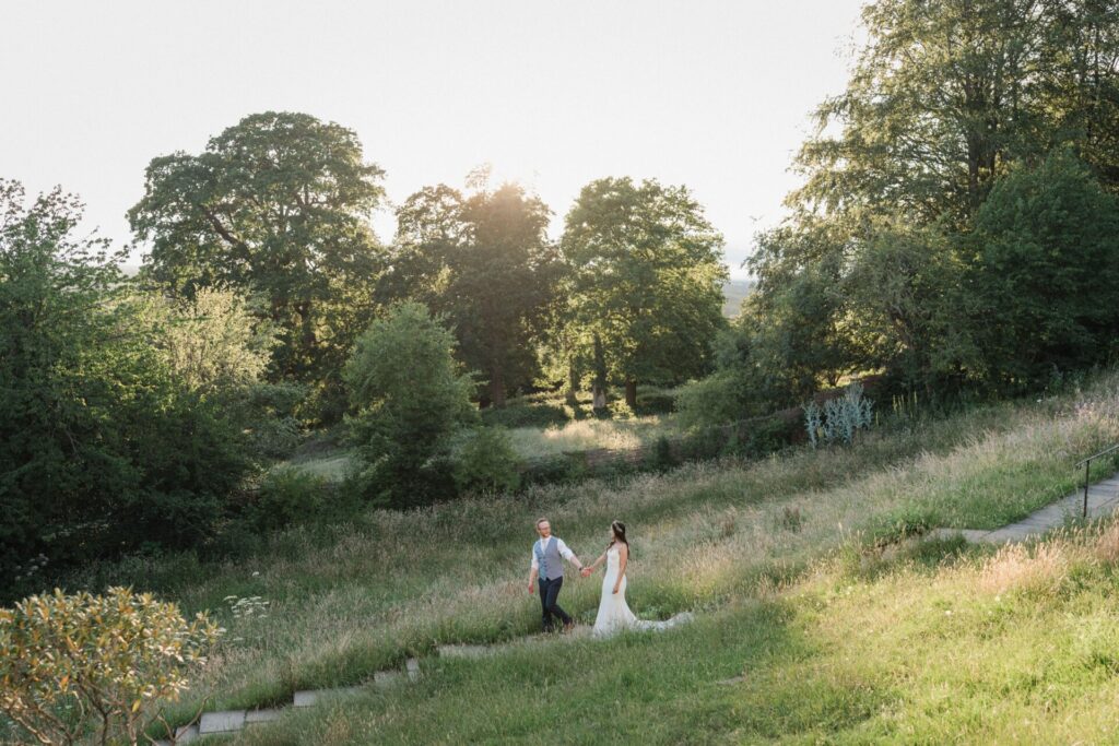 A bride and groom walking through a field at dusk.