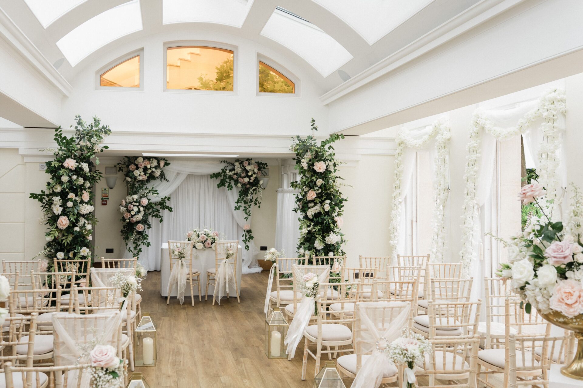 A large bright room with tall floral arrangements and rows of chairs.
